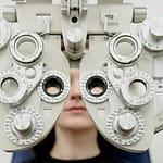 Woman diagnosing vision on refractor testing device during eye examination in modern ophthalmology clinic